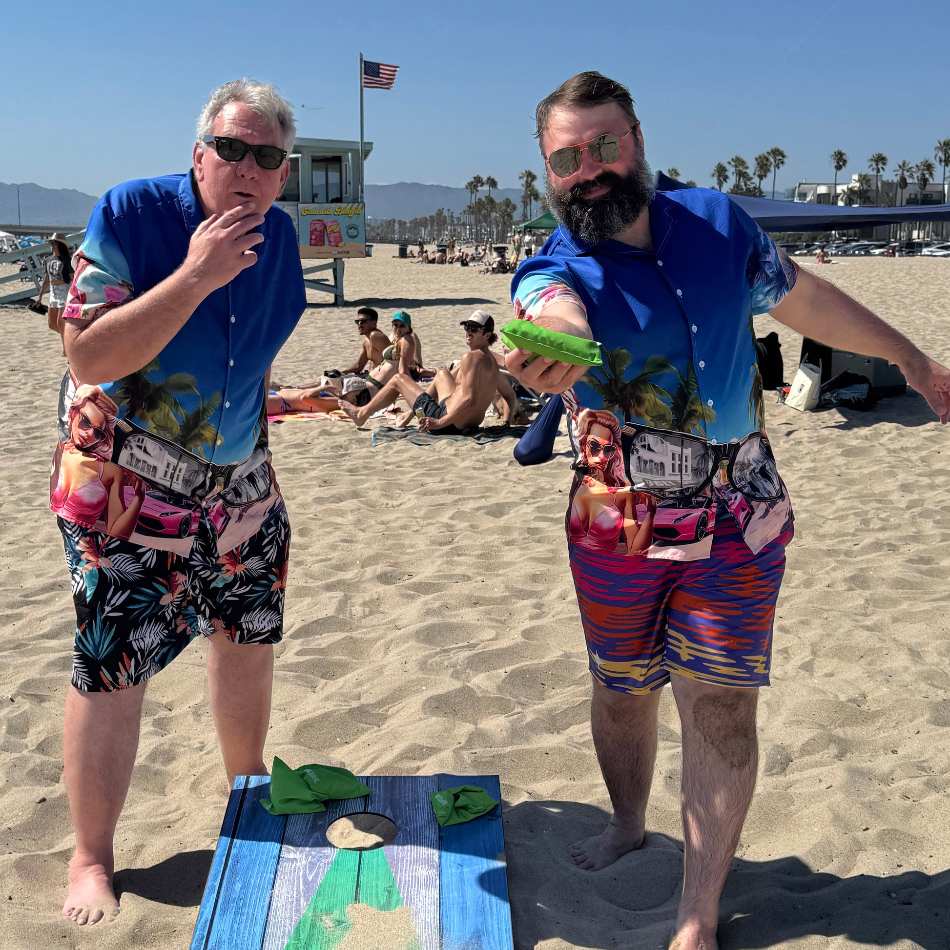 Two guys wearing They Live Miami-flavored Hawaiian shirt atplaying cornhole at the beach