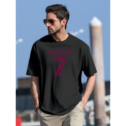 Man wearing a black t-shirt with 'GROUP 7' printed on it, standing outdoors.