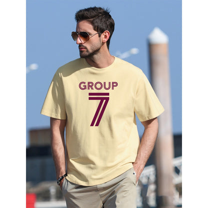 Man wearing a beige t-shirt with 'GROUP 7' printed on it, standing outdoors.