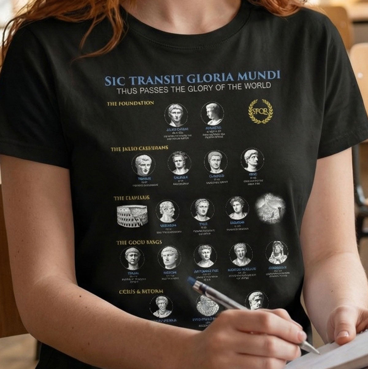 Person wearing a black t-shirt with graphic designs and text, sitting at a table.