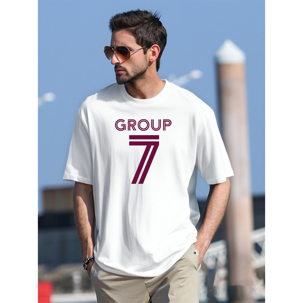 Man wearing a white t-shirt with 'GROUP 7' printed on it, standing outdoors.